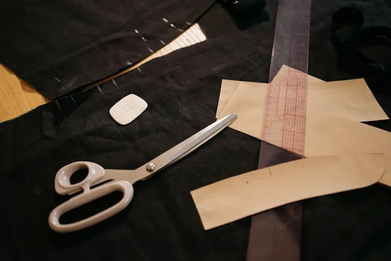 Ciseaux, craie de tailleur, règle et pièces de patron posés sur un tissu noir pour la coupe.
