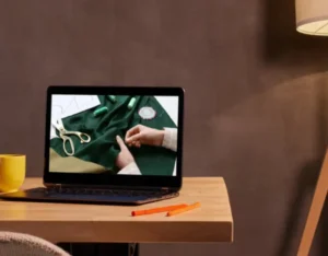 Ordinateur portable sur une table, affichant une vidéo de couture avec du tissu et des accessoires.